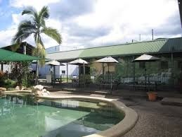 Outdoor swimming pool area with lounge chairs and umbrellas, surrounded by a green building and palm trees.